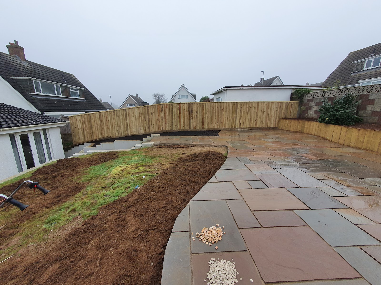 A finished Indian sandstone patio with curved close-board fencing and a retaining wall, built by Createscape