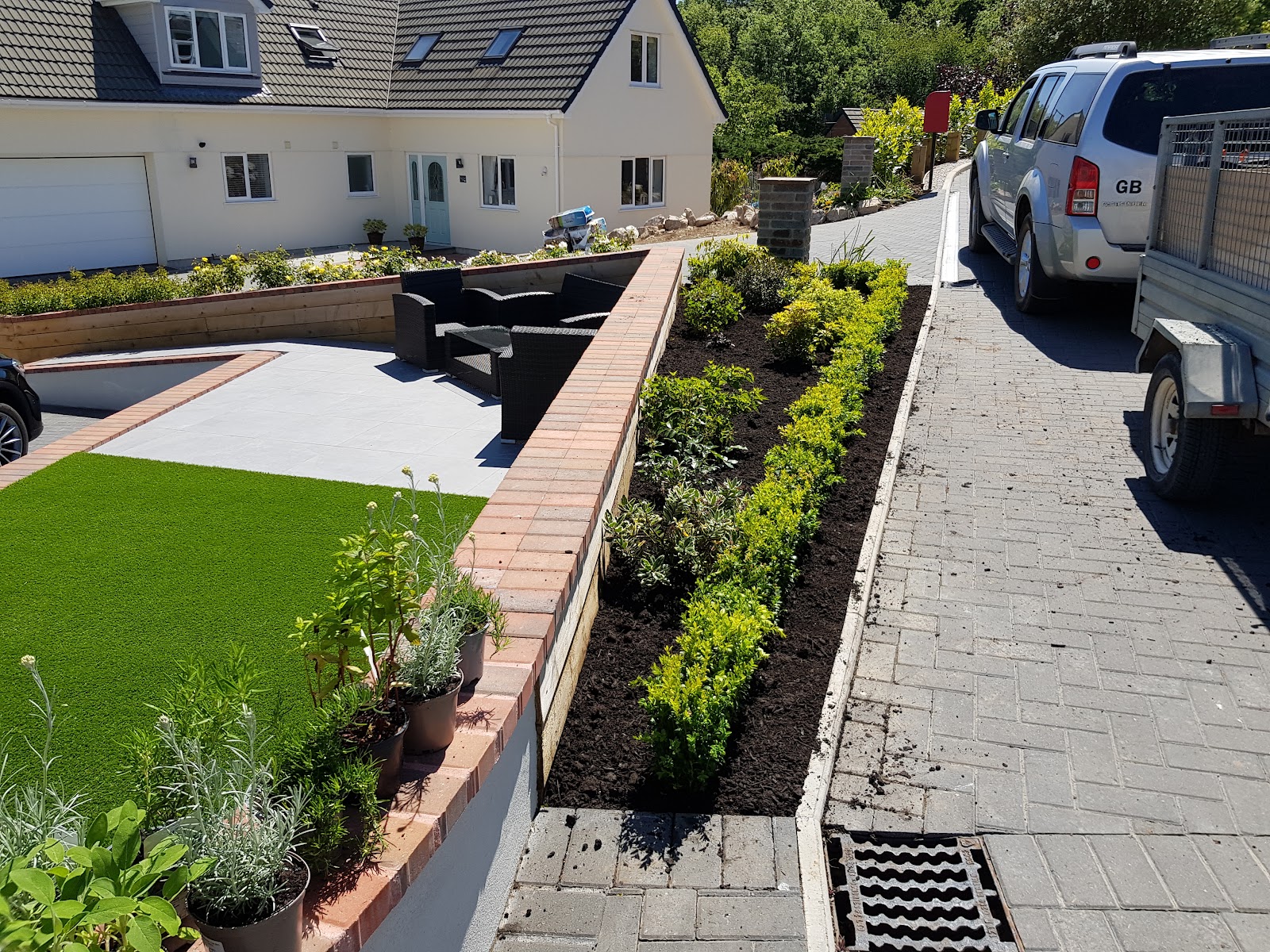 A finished front garden with artificial lawn, raised brick planting beds and a block-paved driveway